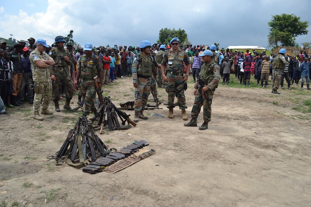 MONUSCO peacekeepers stand around weapons laid on the ground during a handover ceremony in North Kivu, watched by a crowd of residents