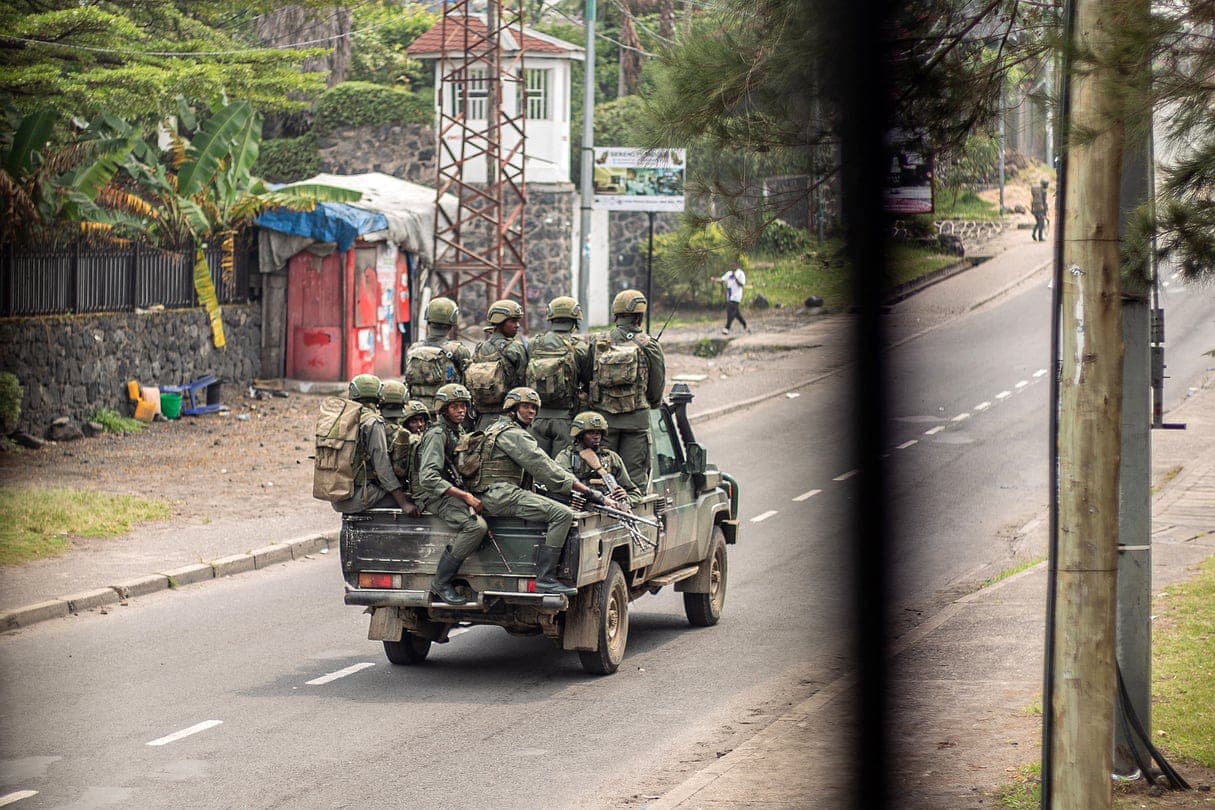Armed men in military fatigues ride in the back of a pickup truck on an avenue in Goma