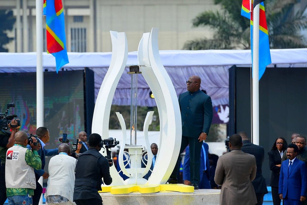 Le président Félix Tshisekedi se tient auprès de la flamme du mémorial du GENOCOST, drapeaux congolais en arrière-plan