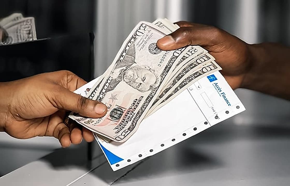 Deux mains échangent une liasse de billets de banque au-dessus d'un bordereau Accès Finance, à un guichet