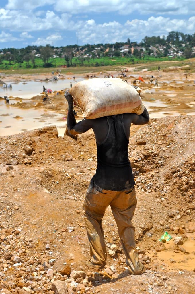 A creuseur carries a sack of copper ore on his shoulder across an artisanal mining site