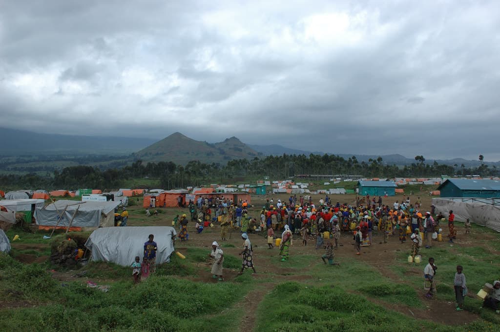 Wide view of a displacement camp in North Kivu, with tarpaulin shelters and the Virunga hills behind